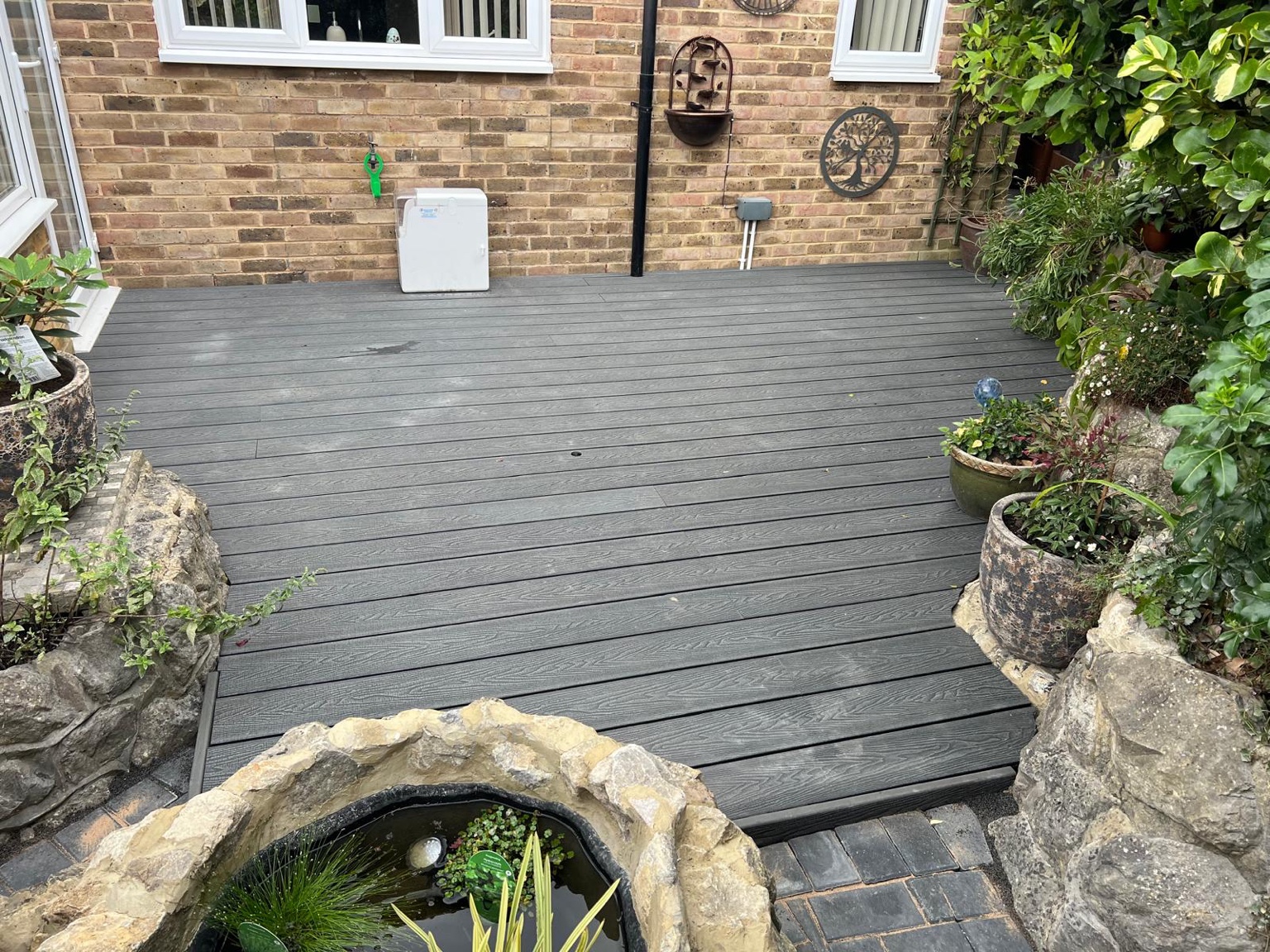 Grey composite decking shaped around ragstone borders in Ashford